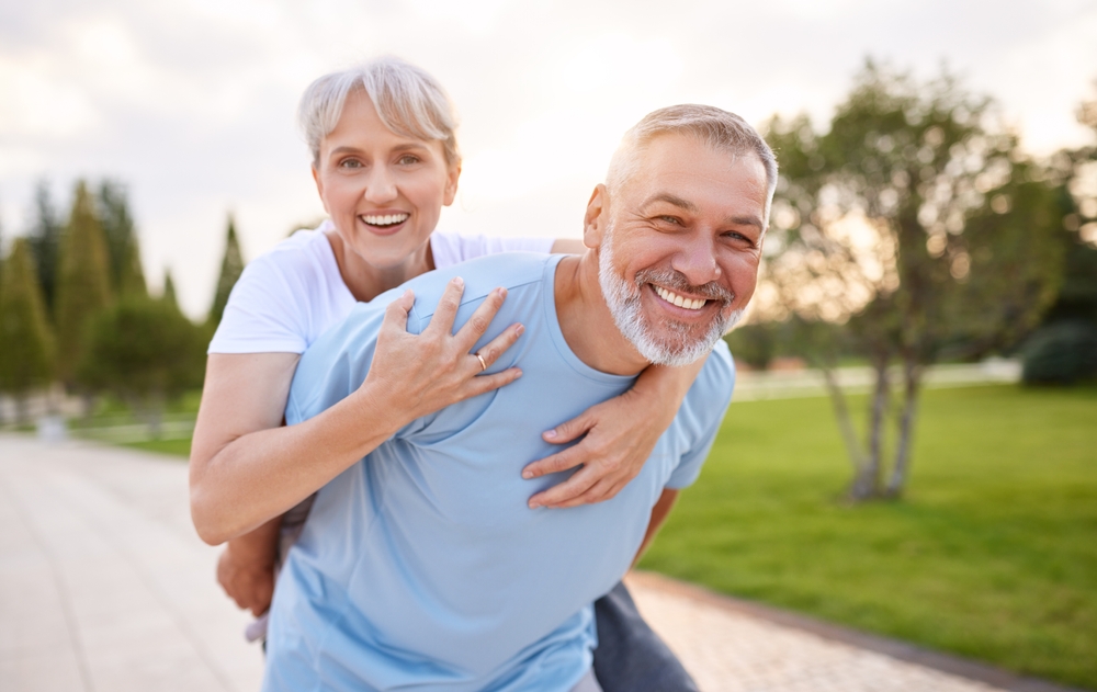 Smiling older couple enjoying a piggyback ride together outdoors in a park.