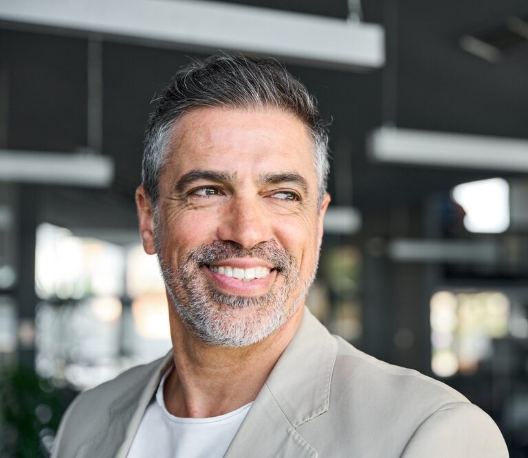 Smiling middle-aged man with gray hair and a beard looks to the side in a modern indoor setting.