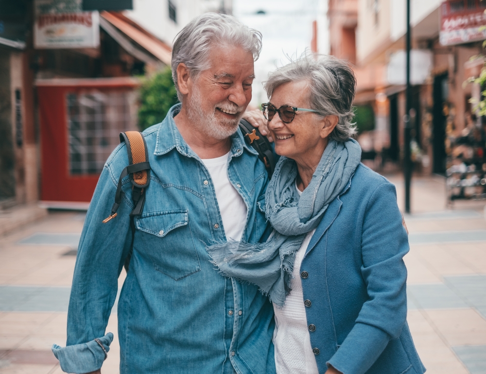 Elderly couple smiling and walking arm in arm down a city street.