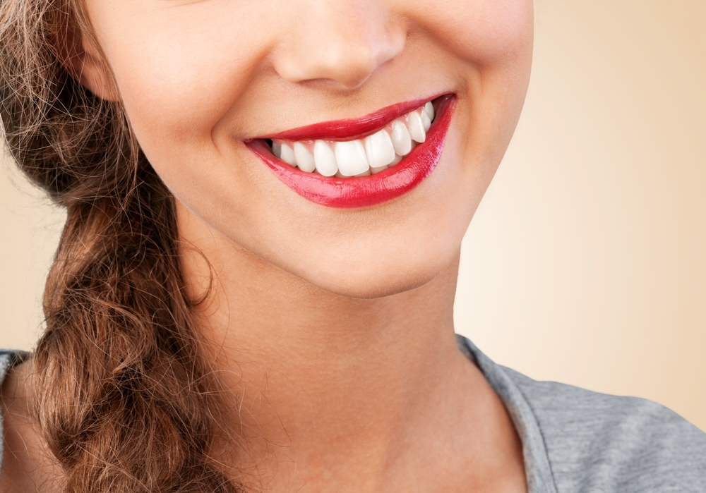 Close-up of a smiling woman’s mouth with bright red lipstick and white teeth, with part of her hair visible to the side.